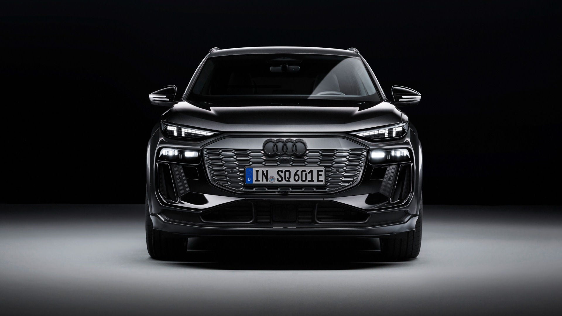 Frontale Ansicht eines schwarzen Audi SQ6 SUV e-tron vor einem dunklen Hintergrund.