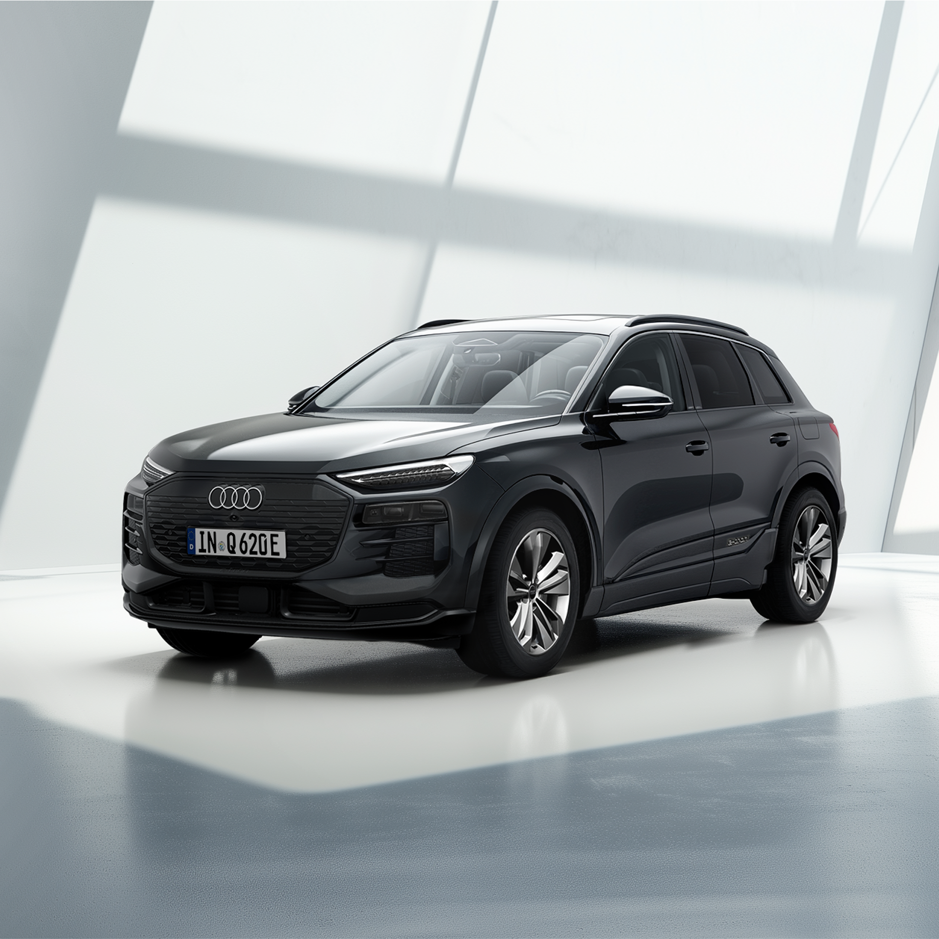 Weißer Audi Q6 e-tron steht am Sandstrand mit Blick auf das Meer und eine felsige Küstenlandschaft im Hintergrund.
