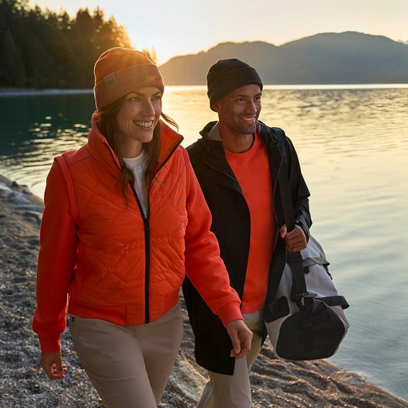 Ein Mann und eine Frau tragen Produkte der Audi collection und gehen an einem Ufer entlang .