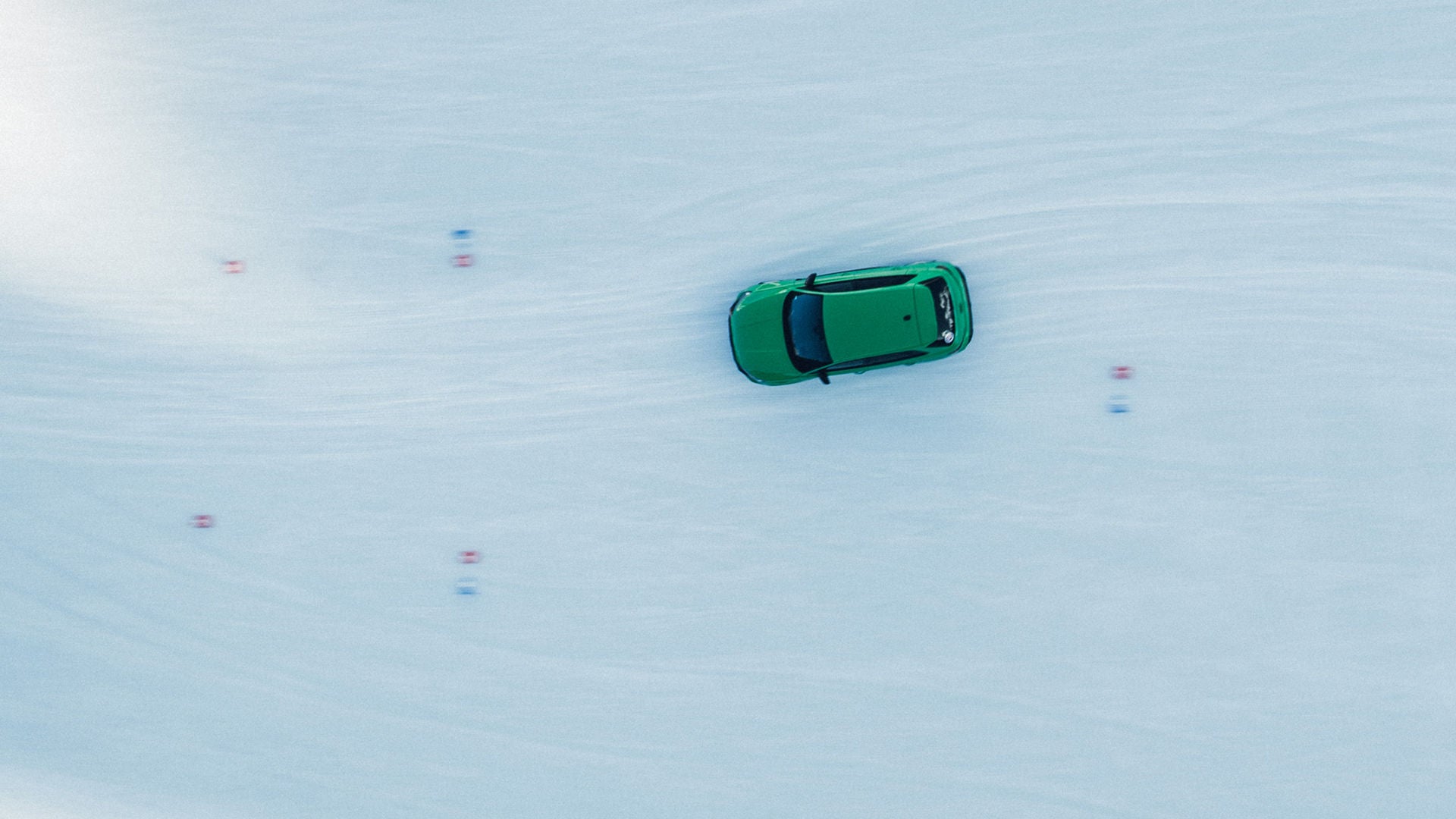Aerial view of a green car on a snow-covered road with lane markings.