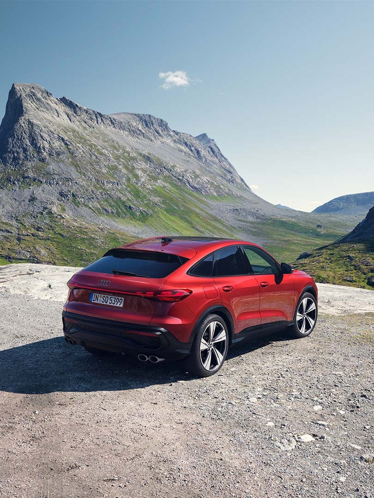 Ein roter Audi SQ5 Sportback von schräg hinten auf felsigem Untergrund in grüner Gebirgslandschaft.