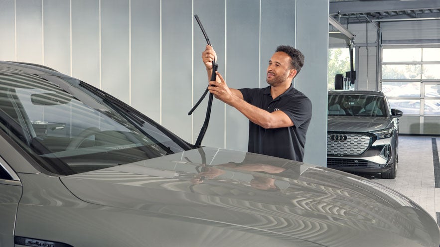 Mitarbeiter in Werkstatt hebt Scheibenwischer eines Audi-Fahrzeugs an zur Wartung oder Kontrolle der Wischerblätter.