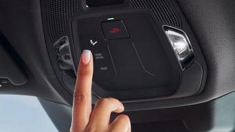 Mann mit Headset sitzt am Schreibtisch in einem Autohaus und arbeitet an einem Computer mit Audi Website, im Hintergrund verschwommen ein Audi.