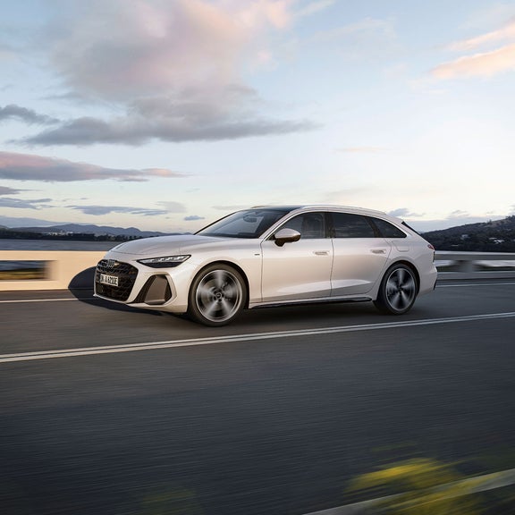 A white Audi A6 Avant e-hybrid cruising on a road