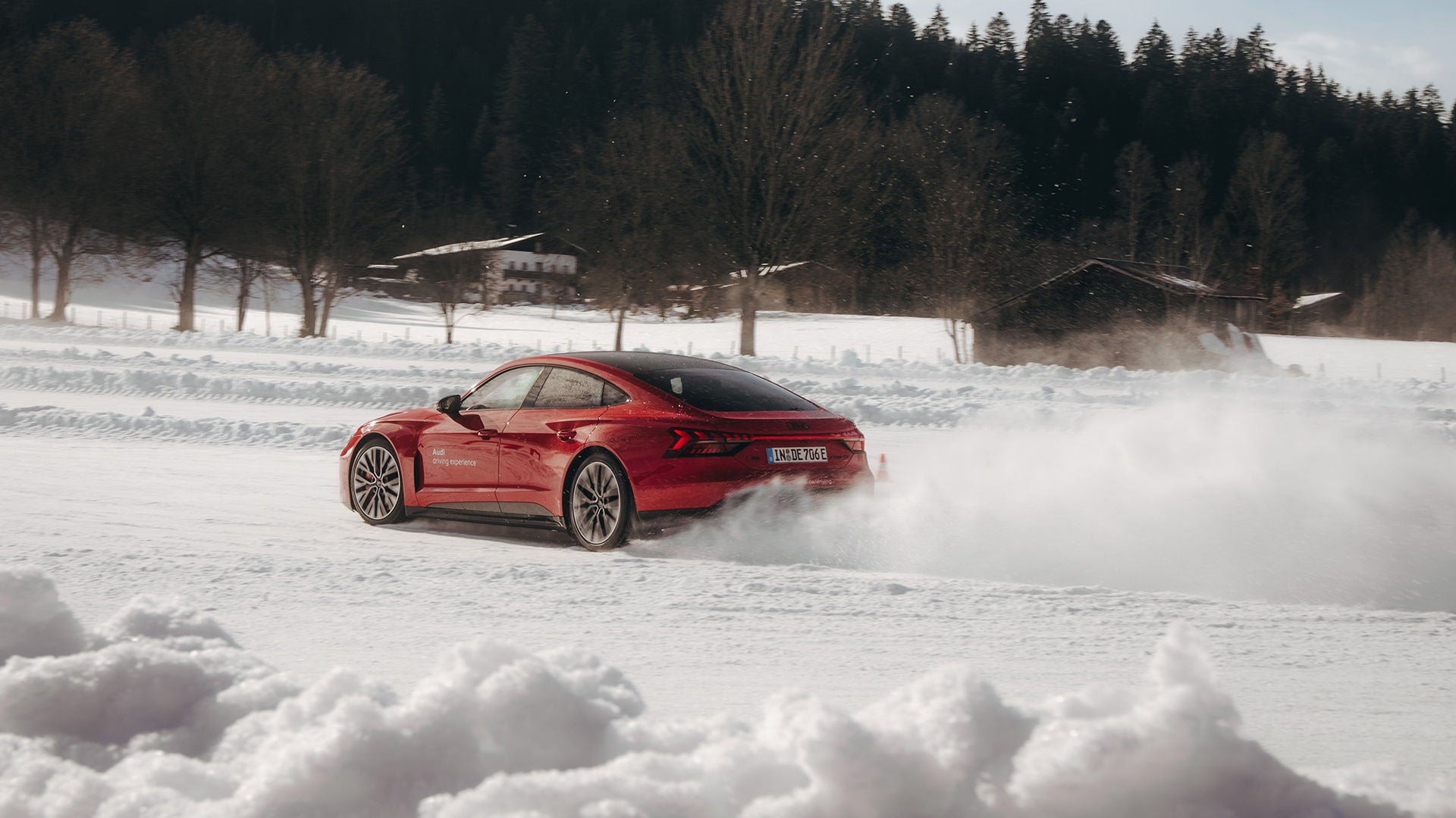 A red Audi e-tron drives along a snow-covered road, snow swirling behind the vehicle.