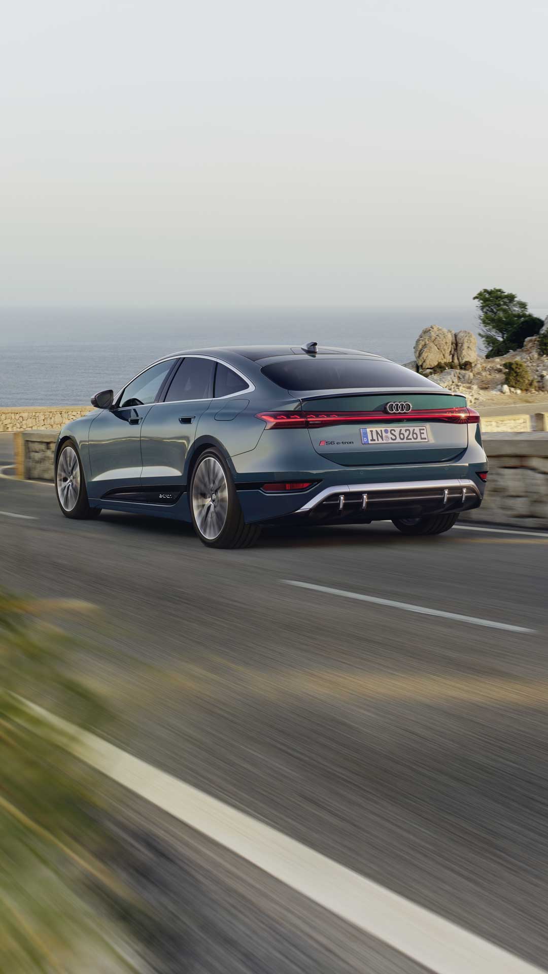 The S6 Sportback e-tron with its sloping rear profile as it drives along a winding coastal road.