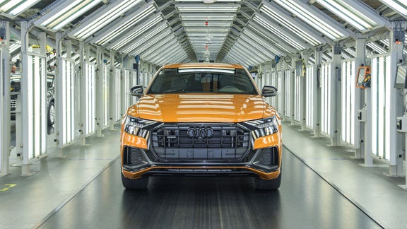 Ein orangefarbener Audi steht in einer hell ausgeleuchteten Fertigungshalle zur Qualitätskontrolle bereit.