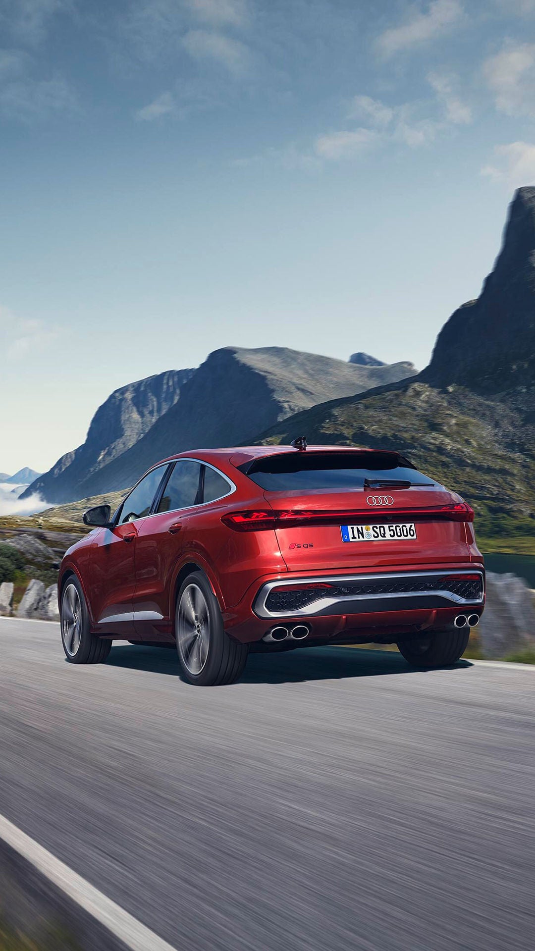 Roter Audi SQ5 fährt auf kurviger Bergstraße mit Felsen und grüner Landschaft im Hintergrund.