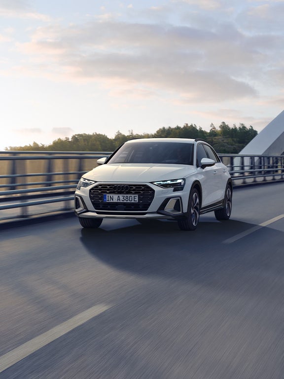 Weißer Audi A3 allstreet TFSI e fährt auf Brücke mit Sonnenreflexion auf der Fahrbahn.
