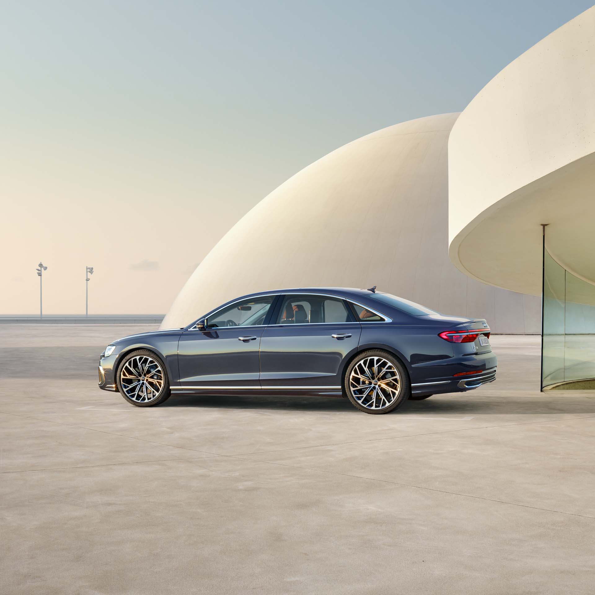 Ein dunkelblauer Audi A8 L steht seitlich vor moderner, heller Architektur bei Tageslicht.