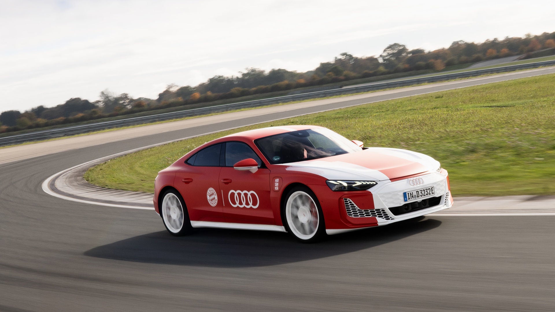 Roter Audi RS e-tron GT FC Bayern Concept mit FC-Bayern-Branding fährt dynamisch auf einer Rennstrecke.