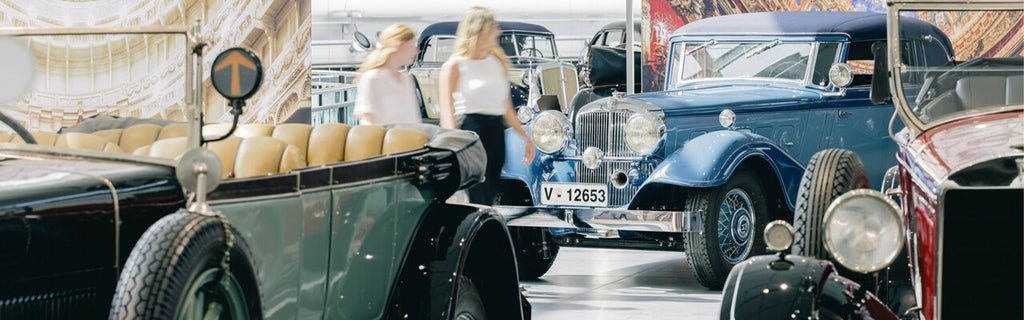 Zwei Frauen gehen durch eine Oldtimer-Ausstellung mit mehreren historischen Fahrzeugen