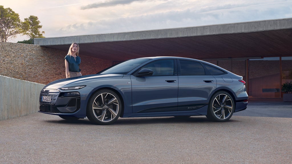 Blauer Audi A6 Sportback e-tron von der Seite, Frau steht daneben vor moderner Garage.