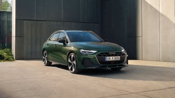 Un Audi A3 Sportback vert foncé est garé devant un bâtiment moderne.