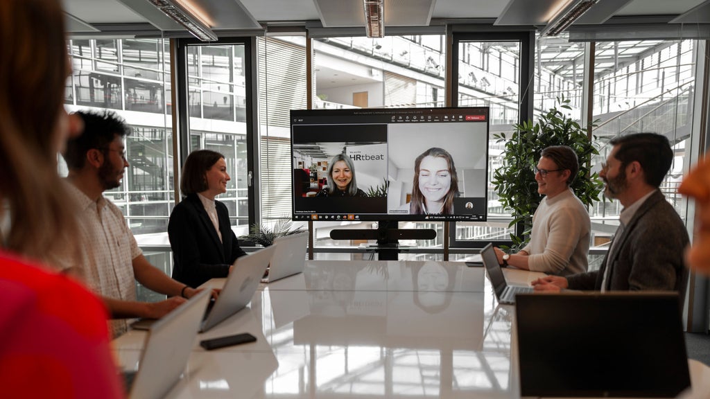 Mehrere Personen sitzen an einem Tisch und haben ein Meeting mit zwei Personen digital am Bildschirm