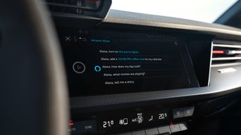 Hand am Lenkrad vor einem Display mit aktivierter Amazon Alexa-Sprachsteuerung im Audi-Cockpit.