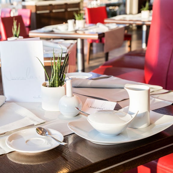 Tables set in a restaurant with white tableware and napkins, seating in red.