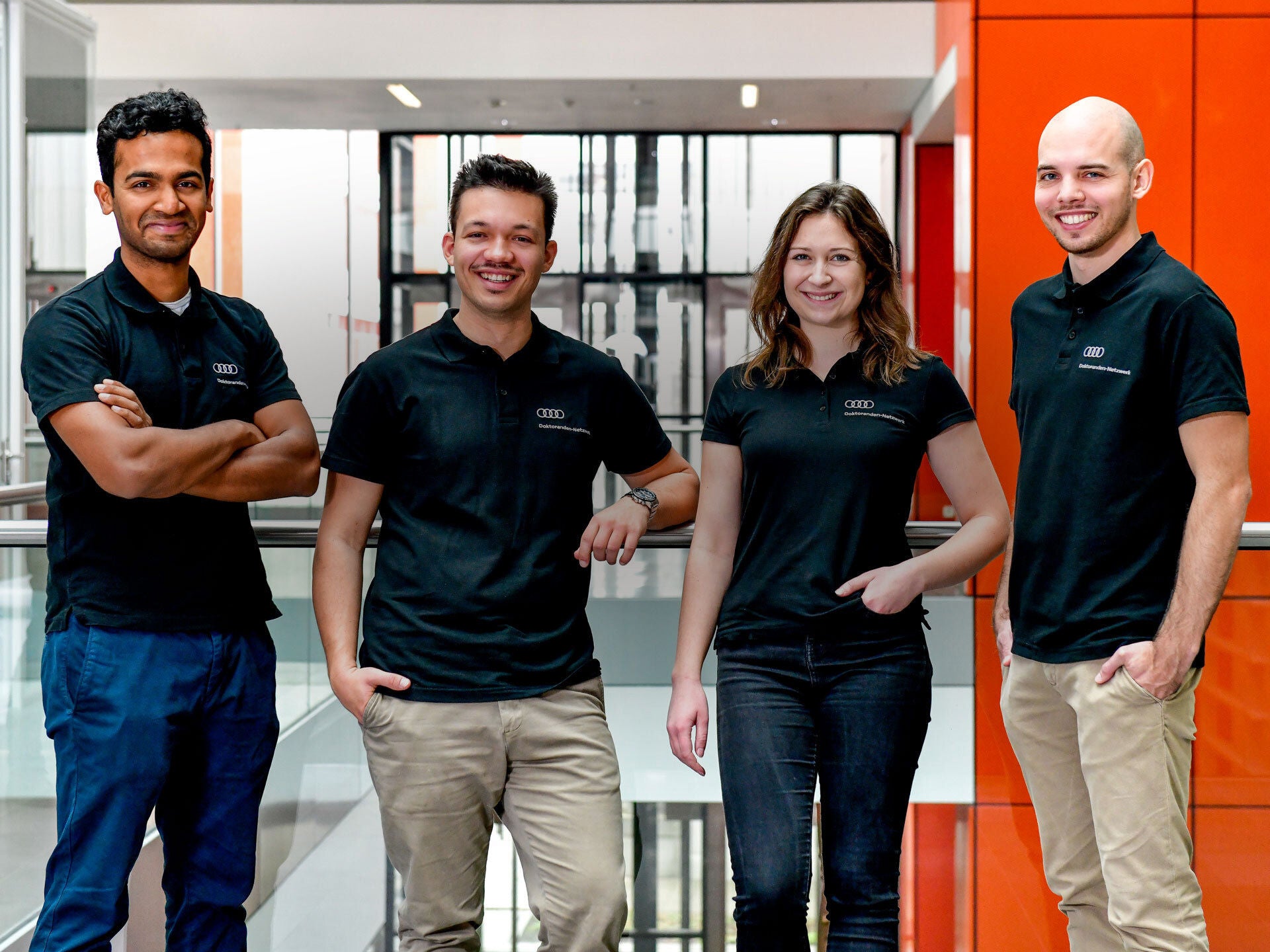 Vier Personen lächeln in die Kamera und tragen dunkle Audi-Shirts