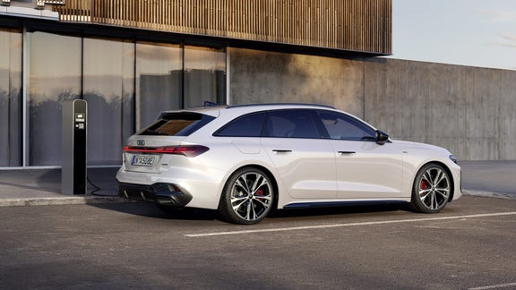 Der A5 Avant e-hybrid steht im schrägen Seitenprofil vor der Fassade eines großen Gebäudes und ist an eine Ladestation angeschlossen.