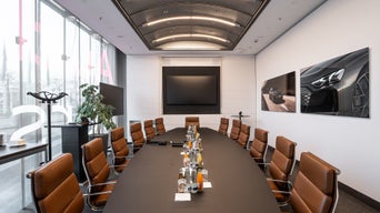 Moderner Konferenzraum mit langem Tisch, braunen Ledersesseln und Getränken auf dem Tisch.