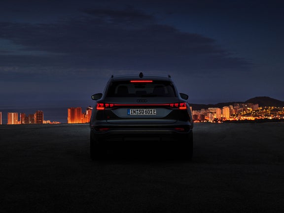 Der Audi Q6 e-tron steht im Dunkeln vor einer beleuchteten Stadt