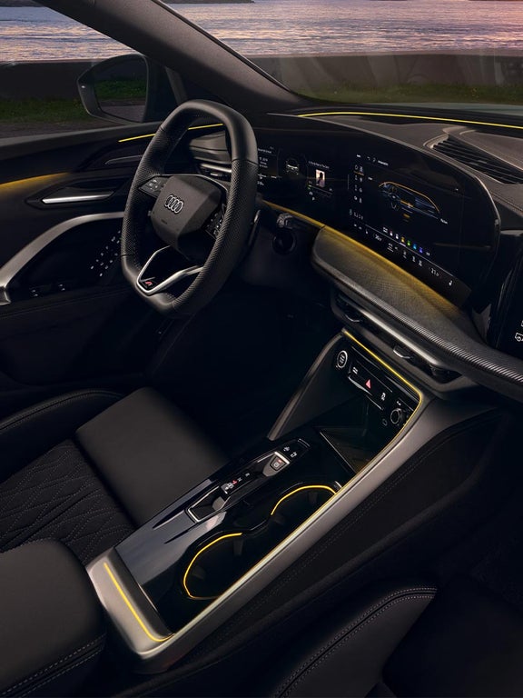 Seitliche Innenansicht des Audi Q5 Sportback mit digitalen Anzeigen und gelber Lichtleiste, Meer bei Sonnenuntergang im Hintergrund.