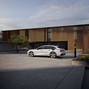 De Audi A6 Avant e-hybrid staat naast een laadpaal voor een modern huis.