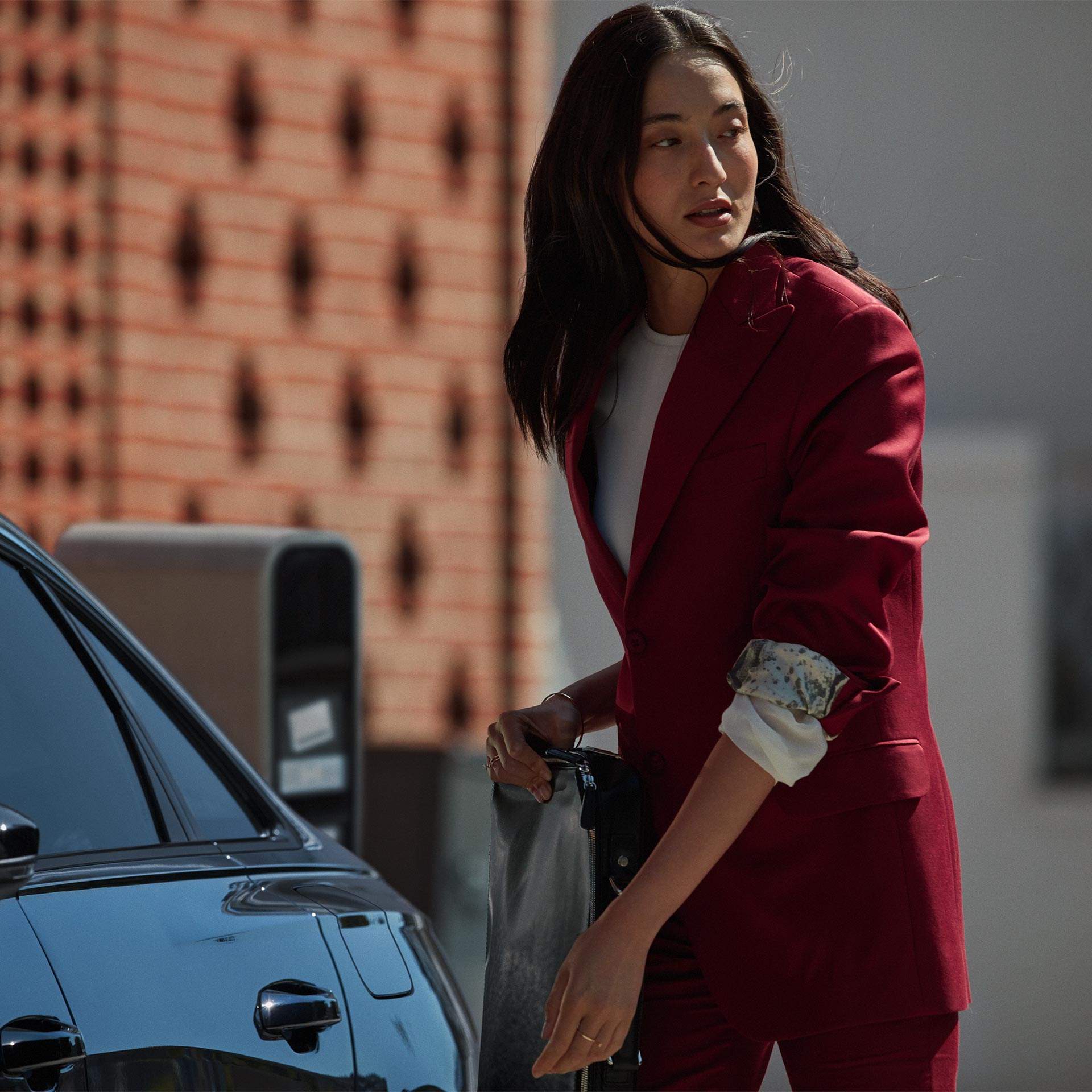 A woman in a red coat walking towards a parked Audi.