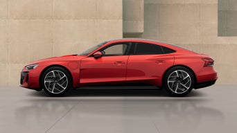 A red electric sedan is showcased against a minimalist concrete background, highlighting its modern design and sporty features.