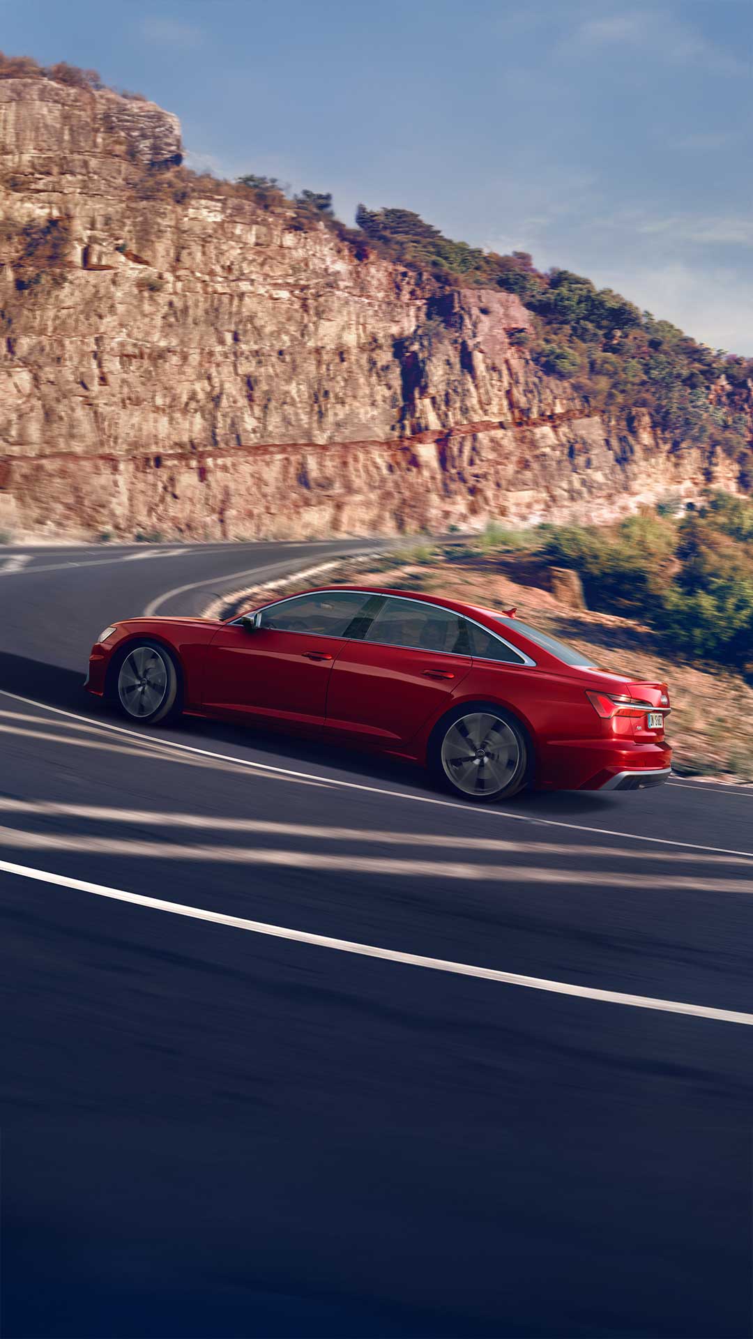 Rote Audi S6 Limousine TDI fährt dynamisch eine kurvige Bergstraße entlang bei sonnigem Wetter.