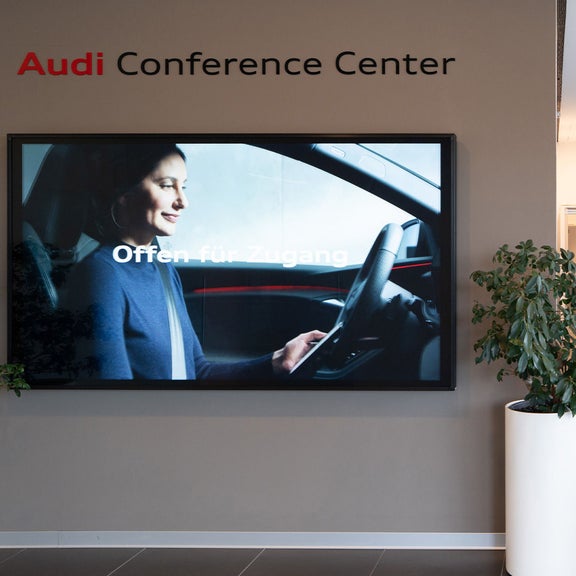 Empfang mit Tresen und Bildschirm im Audi Conference Center, Pflanze im Vordergrund.