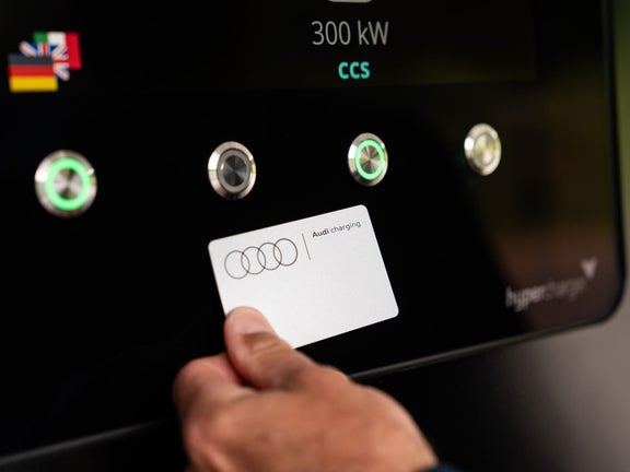One hand holds an Audi Charging card to the NFC surface at the charging hub