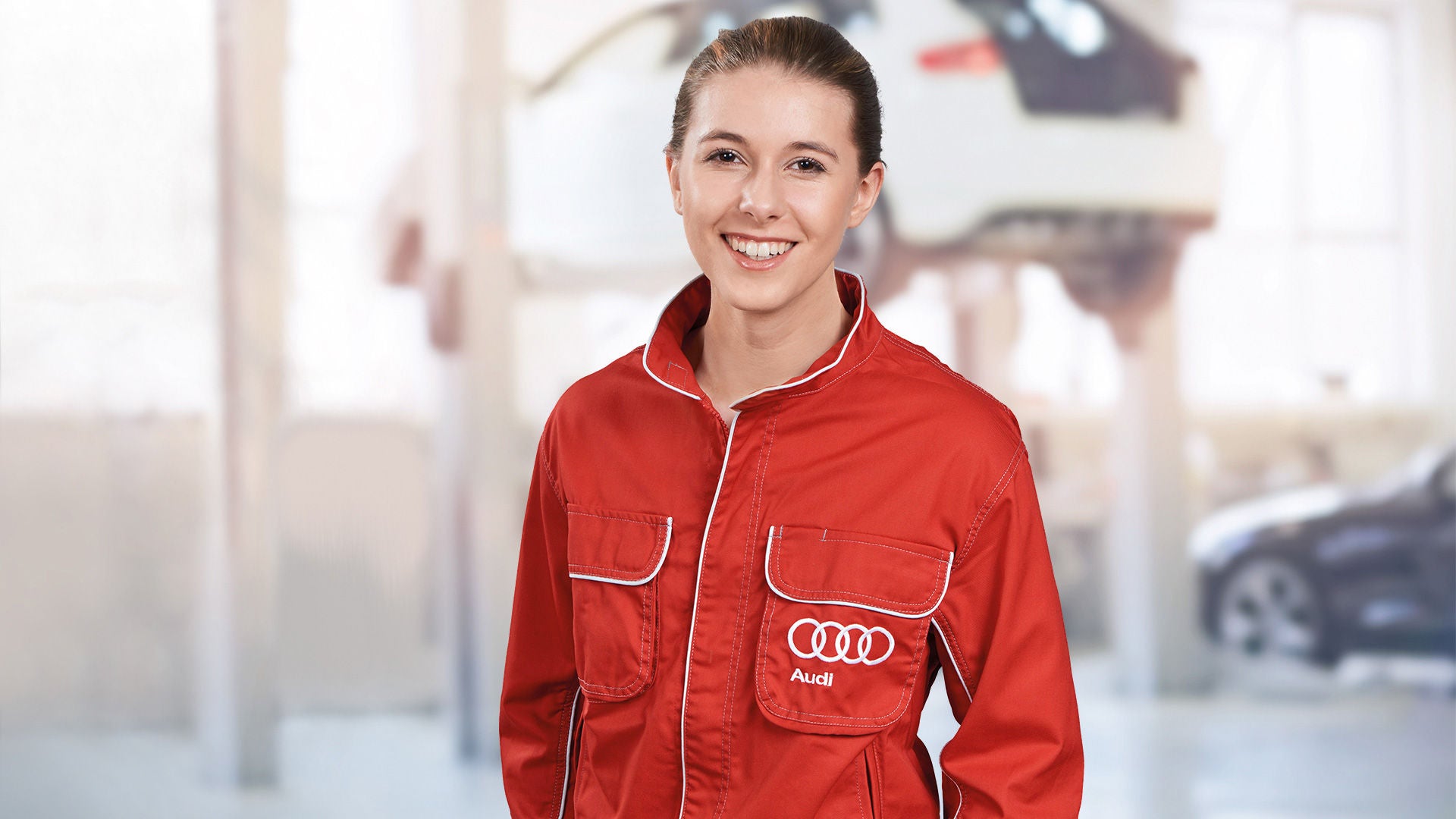 Kfz-Mechatronikerin für Karosserietechnik steht in der Werkstatt und lächelt in die Kamera