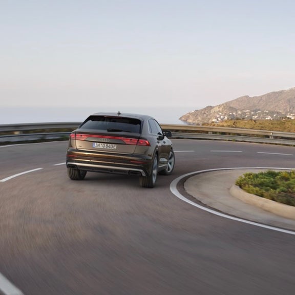 Rear view of Audi Q8 tfsi e turning into a corner travelling along an open road.