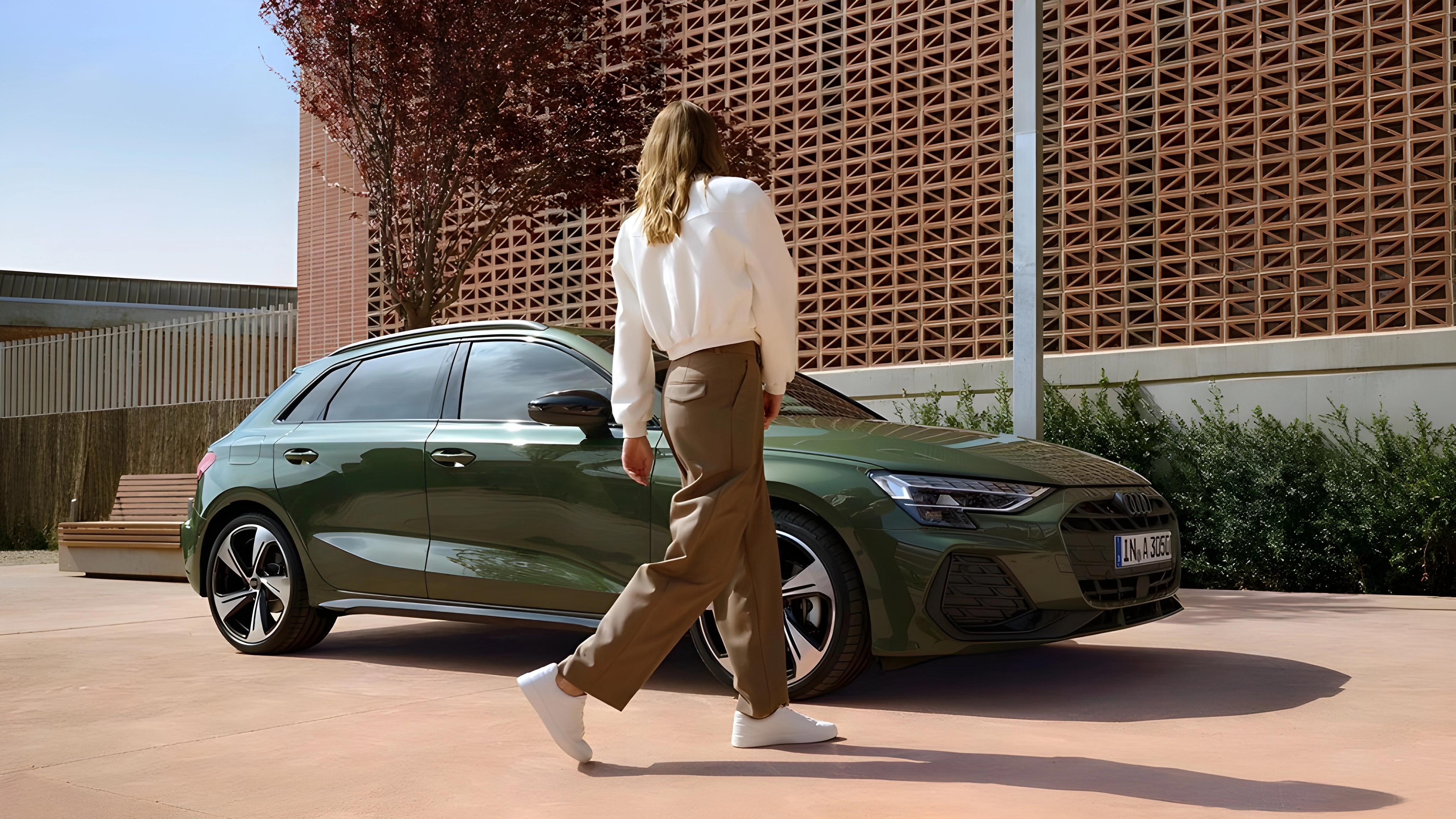 Green Audi A3 Sportback parked on a pink concrete surface with a woman walking past.