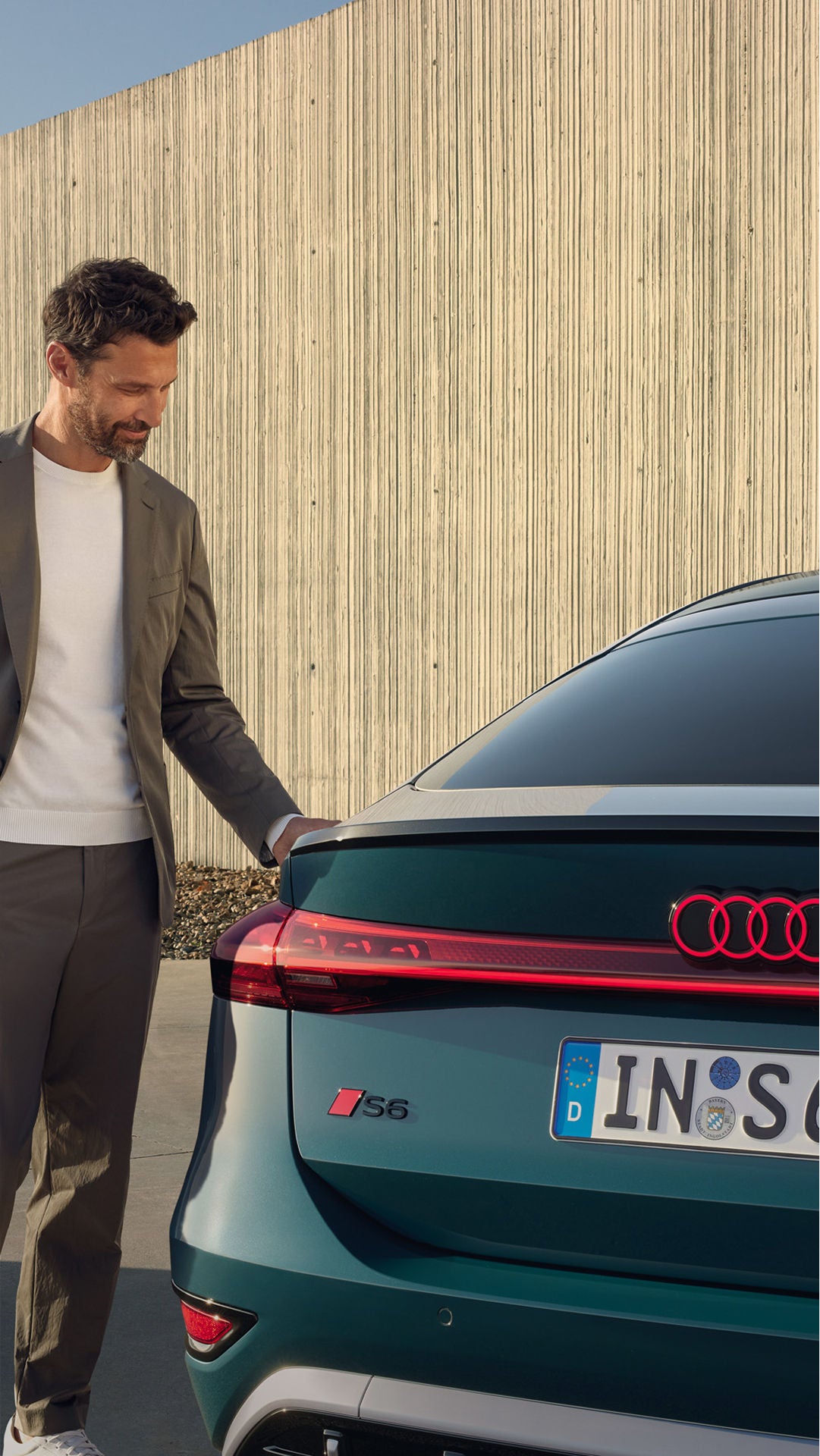 Man stands near a sleek Audi S6 Sportback e-tron, interacting with an electric vehicle charging station against a modern backdrop.