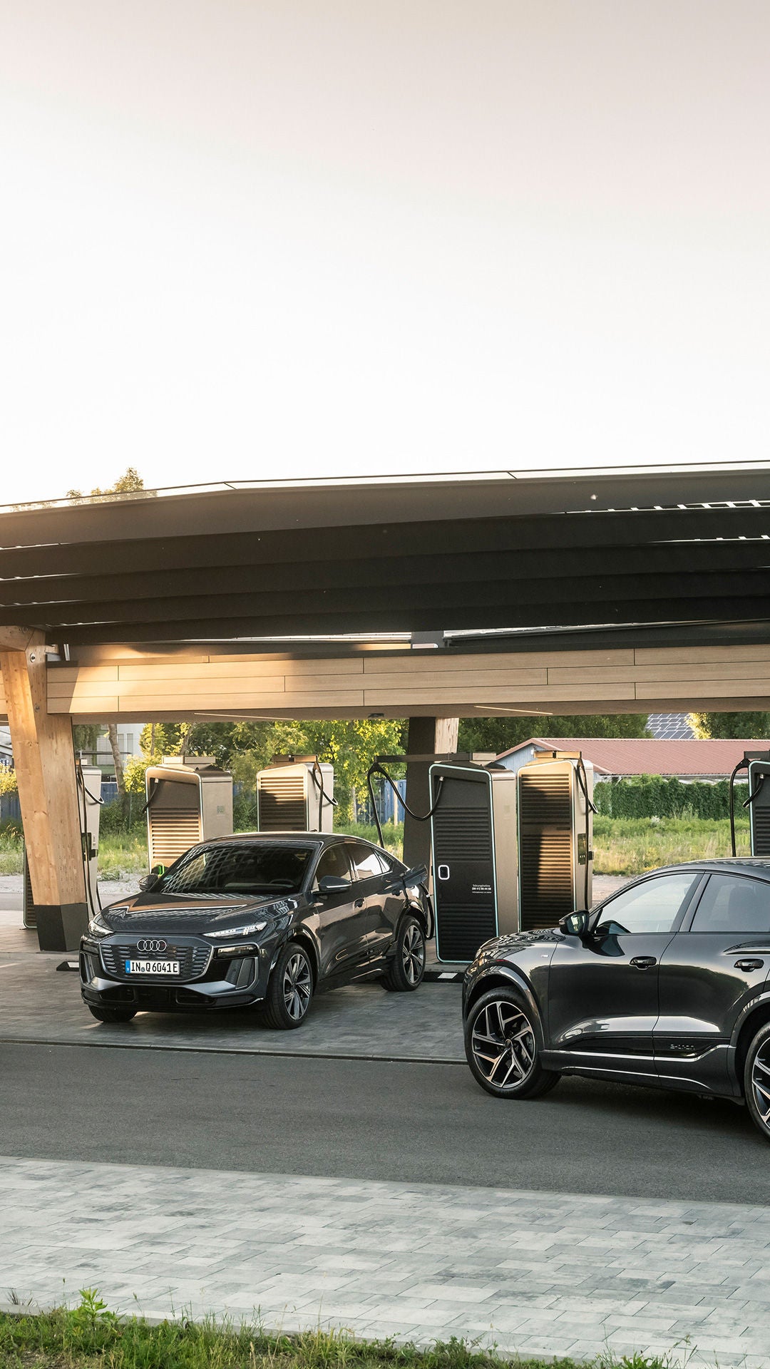 Drei schwarze Audi Modelle parken an einer Ladestation. Das mittlere Audi Modell wird gerade geladen: Im Hintergund geht die Sonne unter.