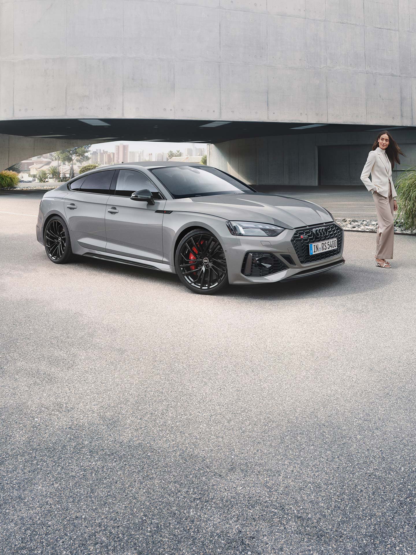 A grey Audi RS5 Sportback car parked outside a building with a person standing beside it.