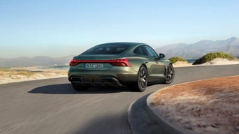 An Audi RS e-tron GT Performance driving on a winding road with a scenic landscape and mountains in the background, showcasing its dynamic design.