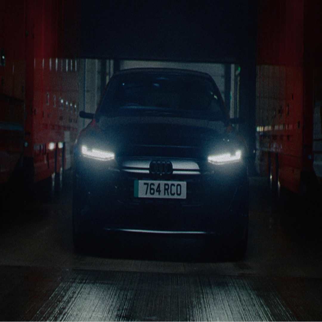 Front view of the all Electric Audi A6 e-tron vehicle exiting a dim garage between red trucks