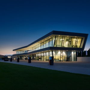 Modernes zweigeschossiges Audi-Gebäude mit Glasfassade und Ladestation, beleuchtet in der Abenddämmerung.