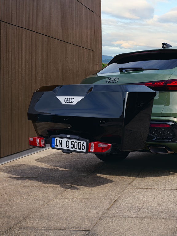 Ein grüner Audi Q5 Sportback mit montierter schwarzer Audi-Transportbox am Heck.