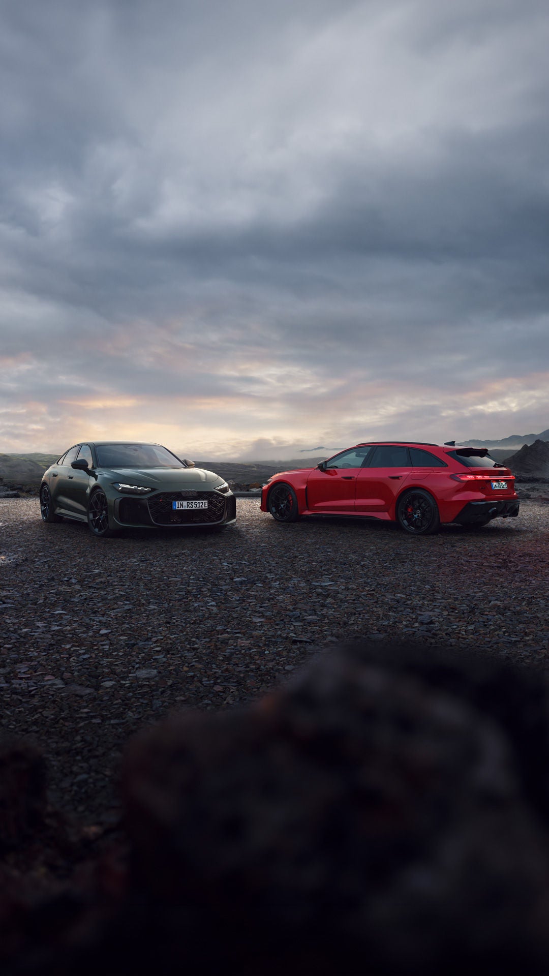 Ein dunkelroter Audi RS 5 Avant und eine dunkelgrüne Audi RS 5 Limousine auf einem einsamen Platz in vulkanisch karger Landschaft. 