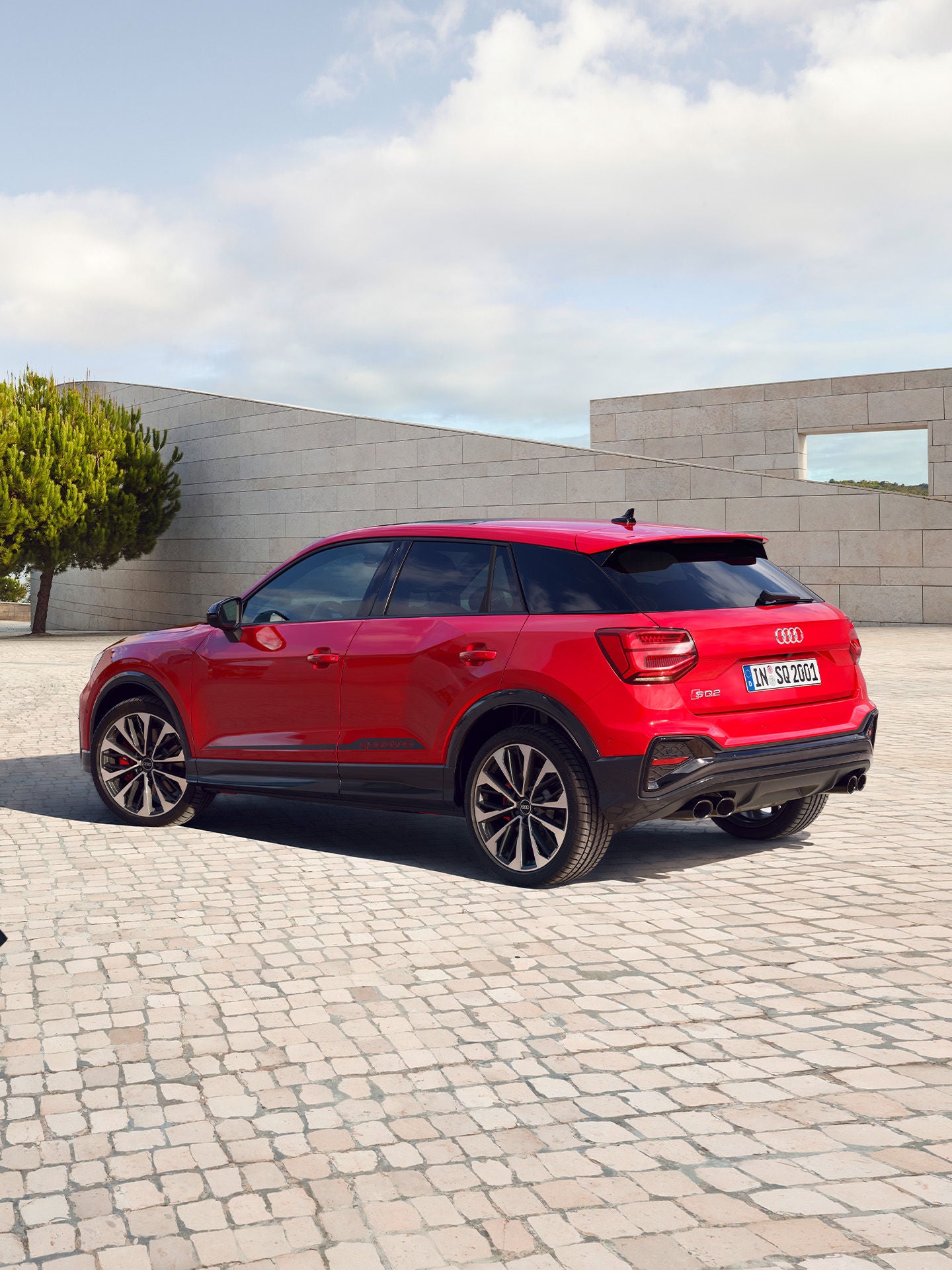 A red Audi SUV parked in a plaza with trees and modern architecture in the background.