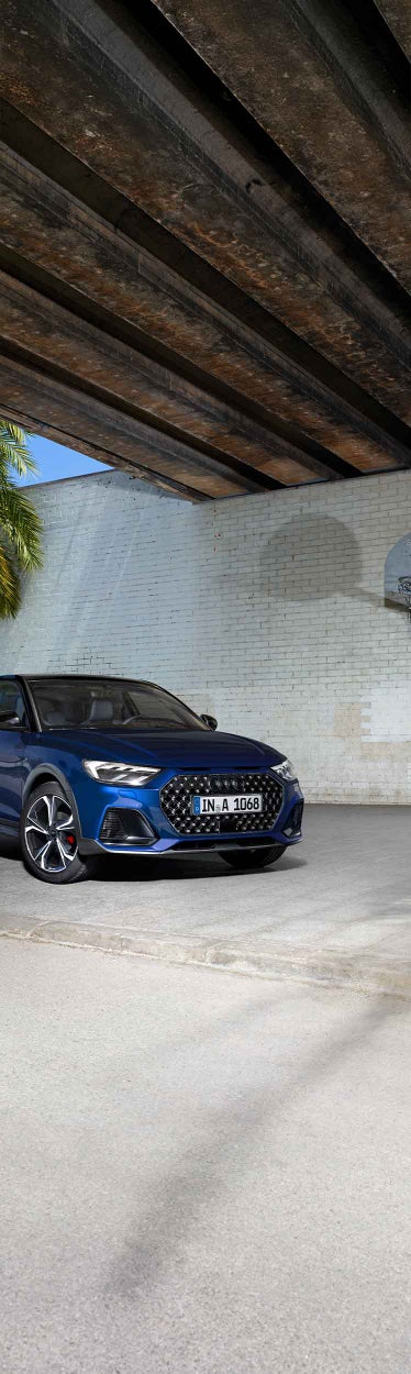 Blauer Audi A1 allstreet schräg von vorne links vor heller Ziegelwand mit sichtbarer Palmenpflanze.