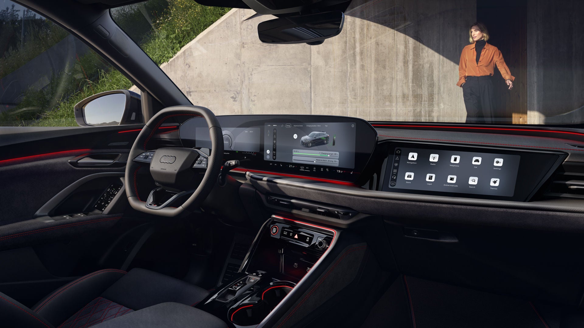 The interior of the Q5 Sportback e-hybrid, with the focus on the steering wheel and the digital displays. A young woman, dressed fashionably, is standing in front of the car.