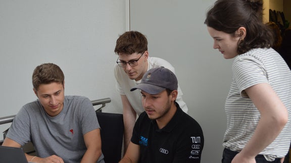 Four persons are looking at a laptop on the table