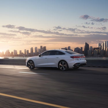 Dynamisch zijaanzicht van de Audi A5 Berline e-hybrid in een straat met een grote stad op de achtergrond