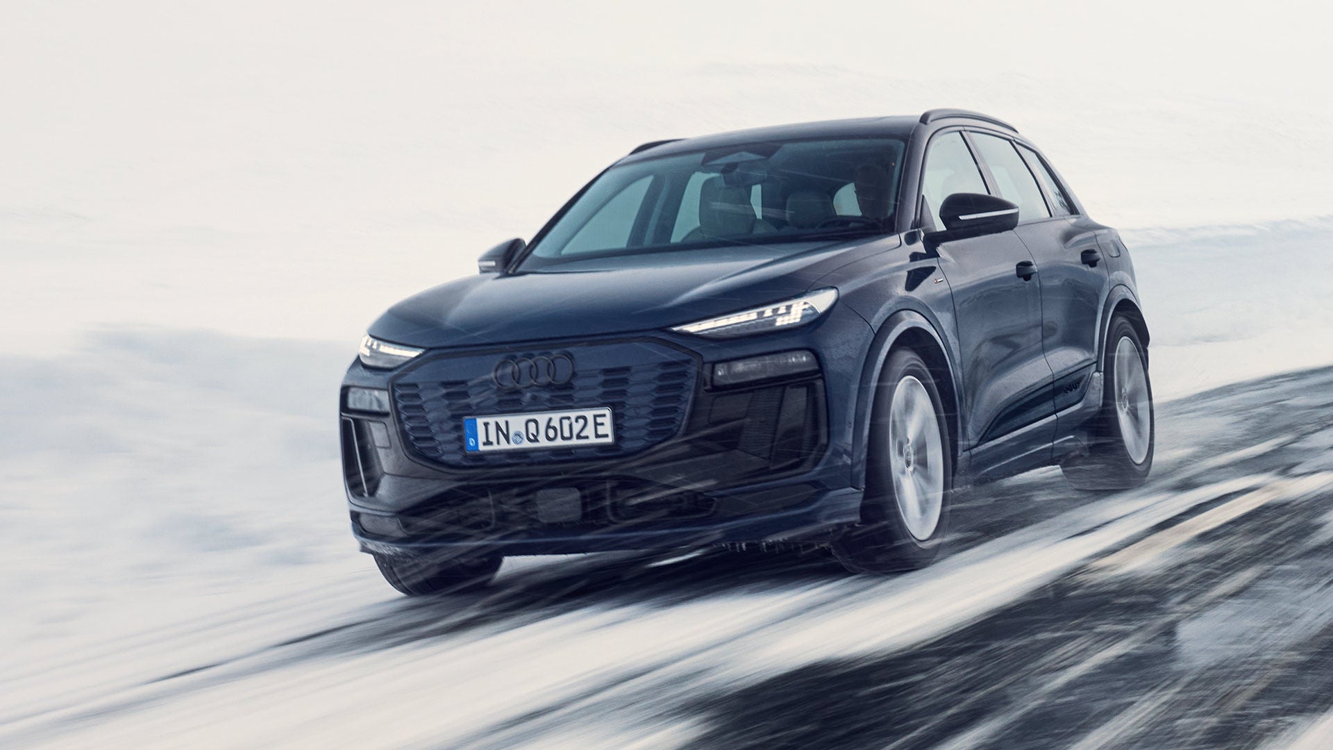 Ein schwarzer Audi Q6 SUV e-tron fährt auf schneebedeckter Straße bei winterlichen Bedingungen.