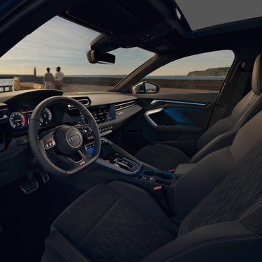 Blick in den Audi-Innenraum mit Lenkrad, Displays und blauer Ambientebeleuchtung bei Sonnenuntergang.